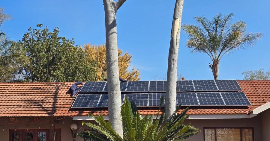 Solar array on a tiled house roof behind palm trees