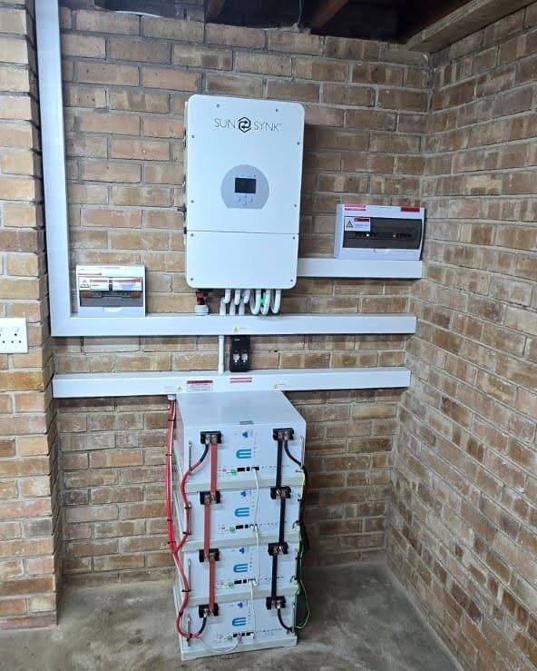 Wall-mounted inverter above a stack of batteries on a brick wall